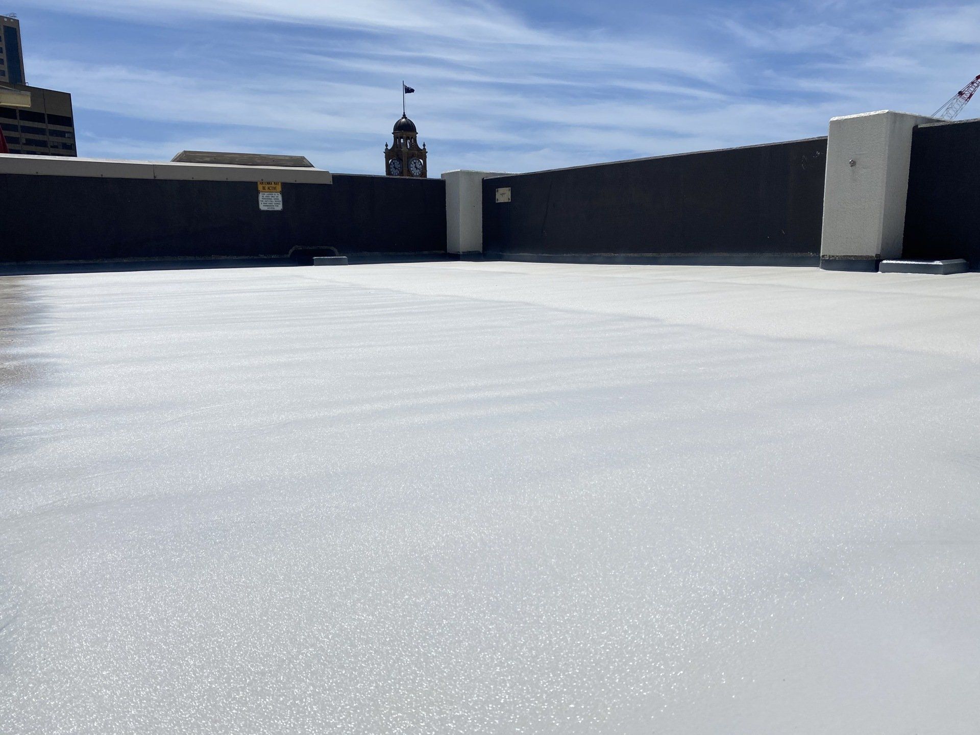White-coated flat roof, dark wall, city skyline background, sunny day. — Unique Waterproofing Solutions in North Rocks, NSW