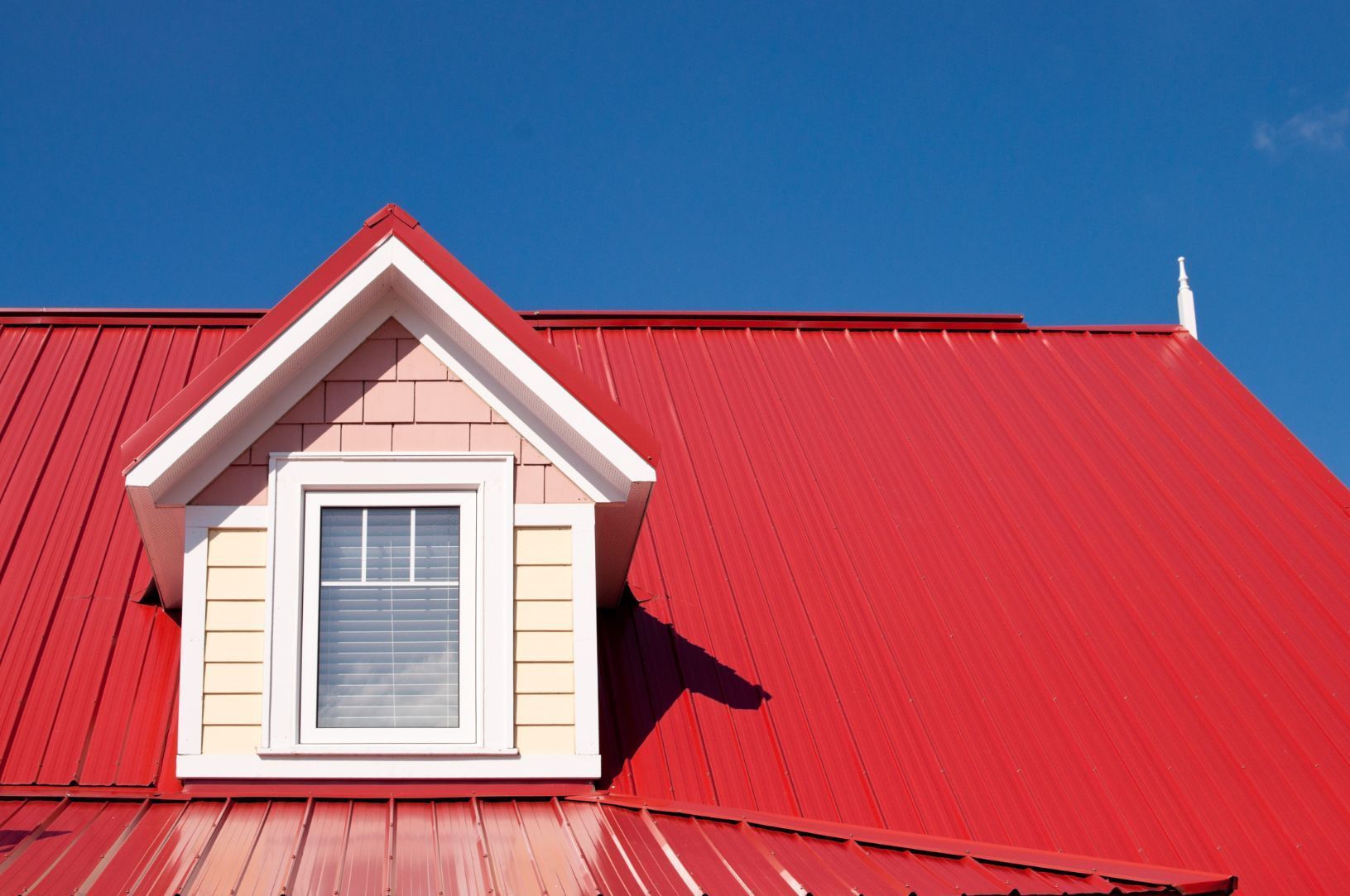 Red metal roof with dormer window against a bright blue sky. — Unique Waterproofing Solutions in North Rocks, NSW