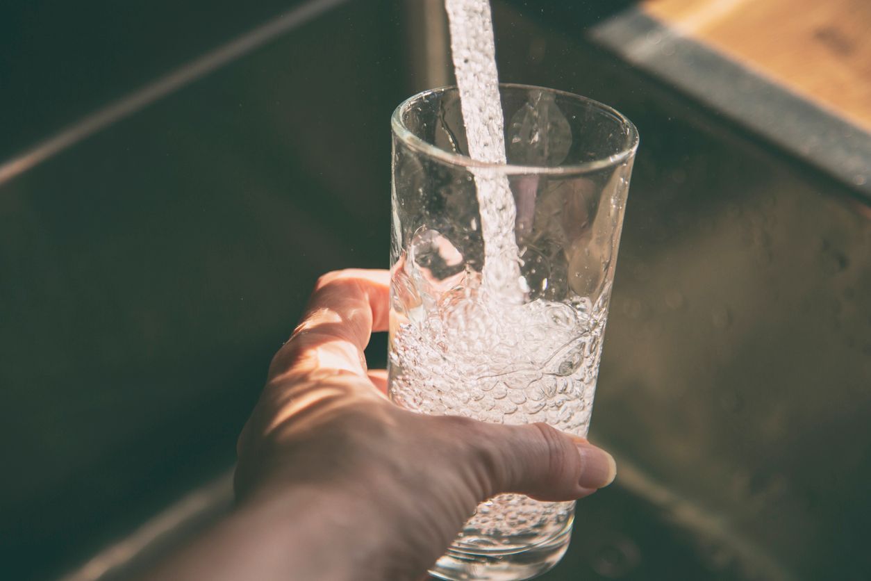 A person is pouring water into a glass in a sink.