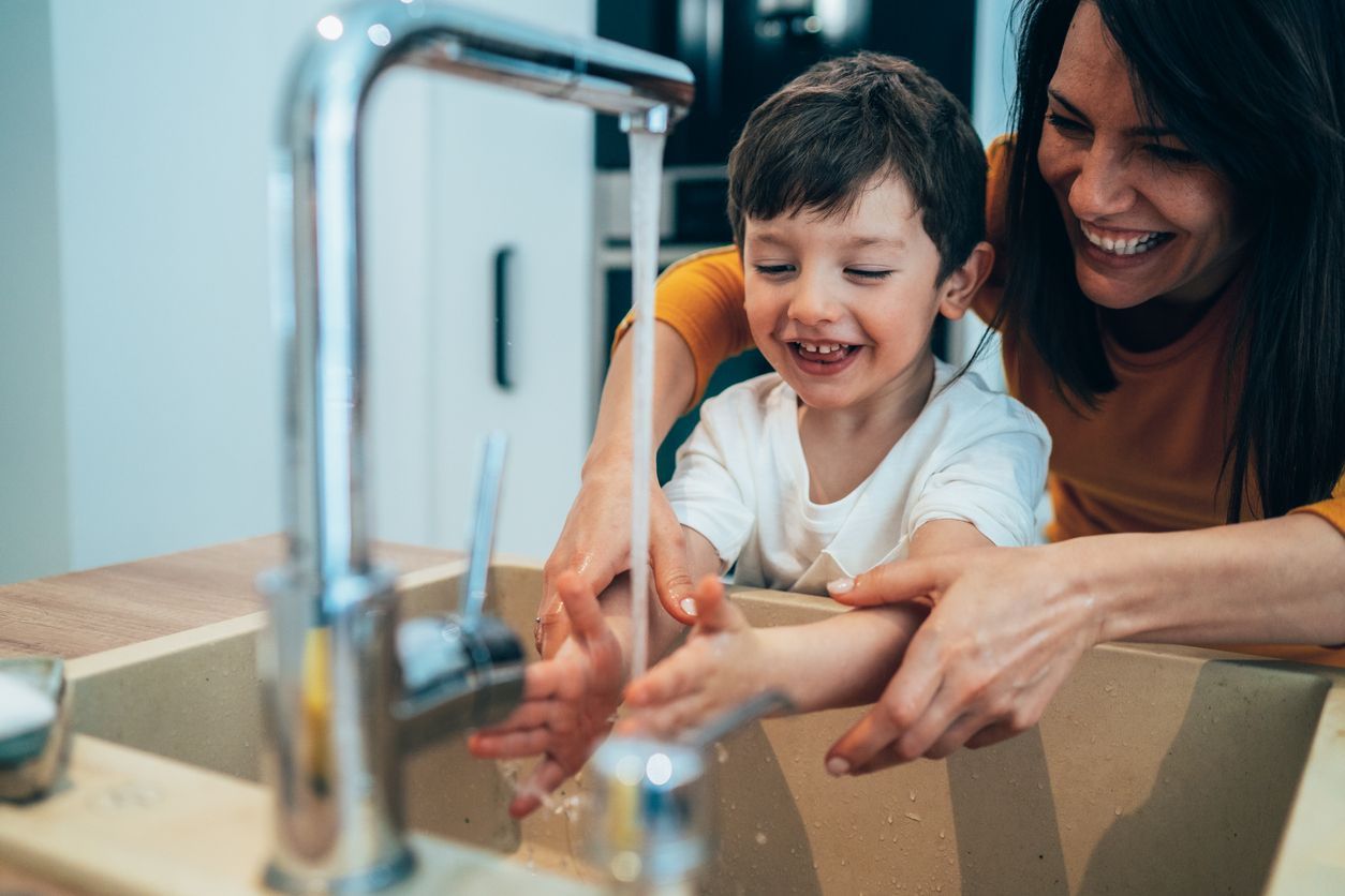 A woman and a child are washing their hands in a kitchen sink.