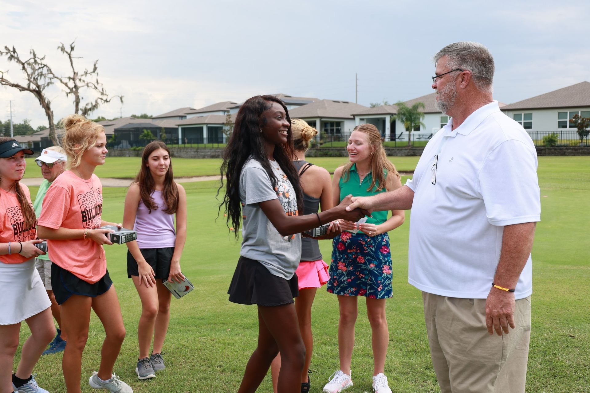 A group of young girls are shaking hands with a man on a golf course.