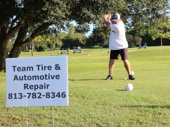 A man is swinging a golf club in front of a sign that says team tire & automotive repair