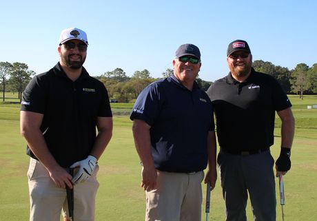 Three men are standing on a golf course holding golf clubs.