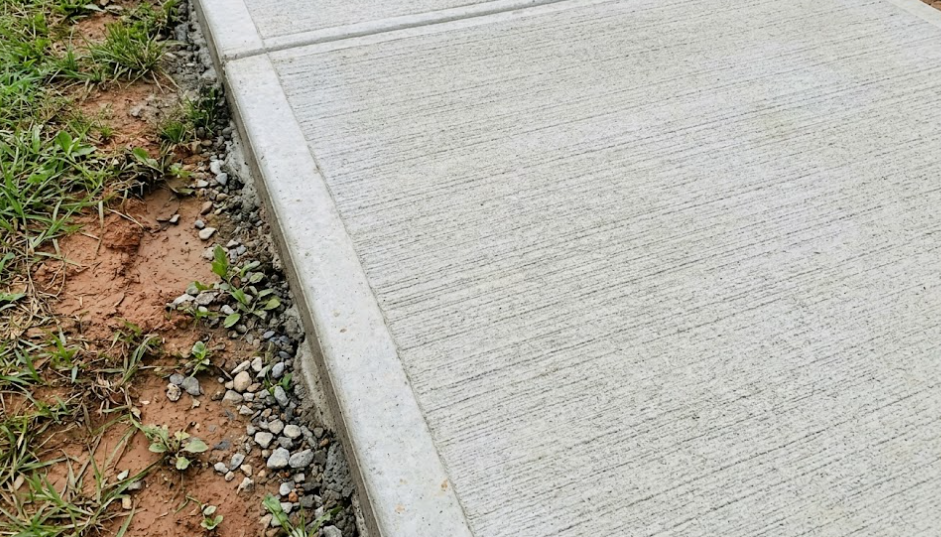 A concrete sidewalk edge with a finished, smooth border next to a strip of dirt, gravel, and grass.