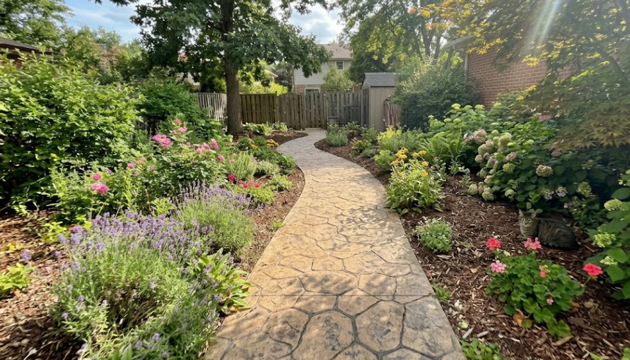 Decorative stamped concrete sidewalk with a stone pattern in a garden setting.