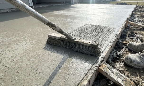 A concrete contractor applying a broom finish to a wet concrete sidewalk for safety and grip.