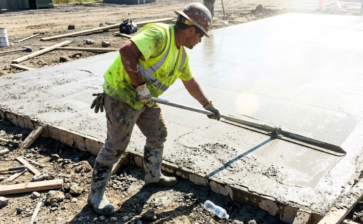 Professional concrete contractor smoothing out wet concrete on a new job site.