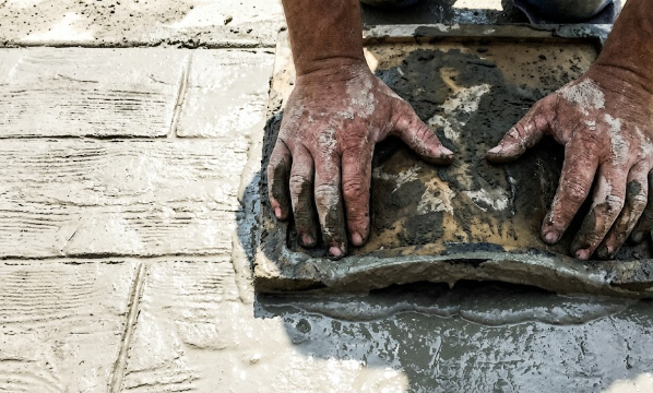 Professional contractor stamping a realistic wood plank pattern into wet concrete.