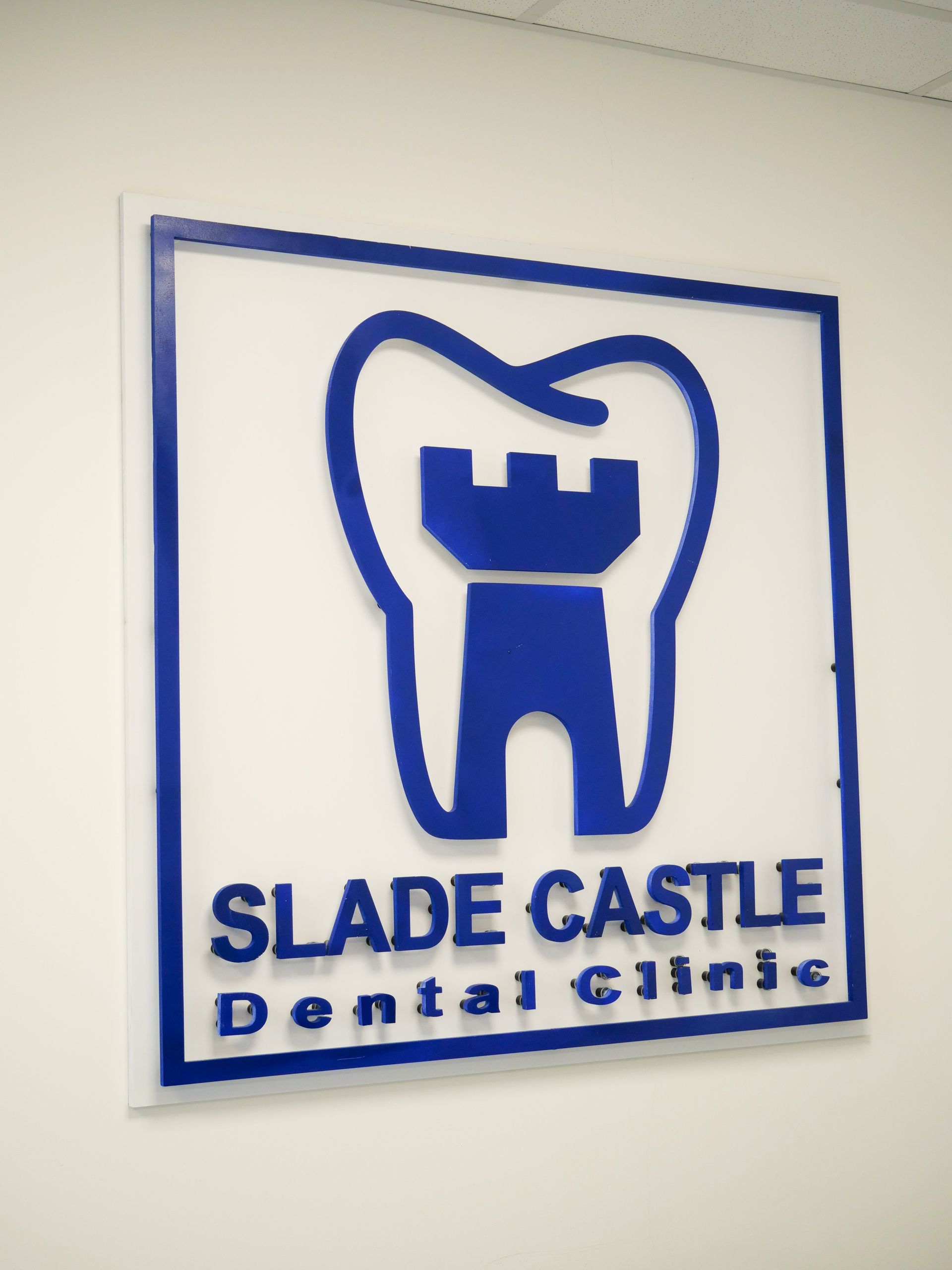 A sign for slade castle dental clinic hangs on a white wall