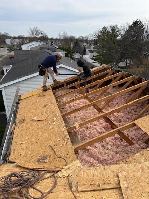 Roofers removing plywood sheathing on a damaged roof during repairs