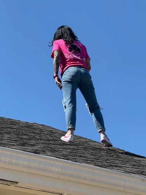 Person in a pink shirt and jeans standing on a roof against a blue sky