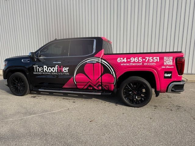 Pink-and-black roofing company pickup truck with “The Roofher” logo parked by a corrugated wall