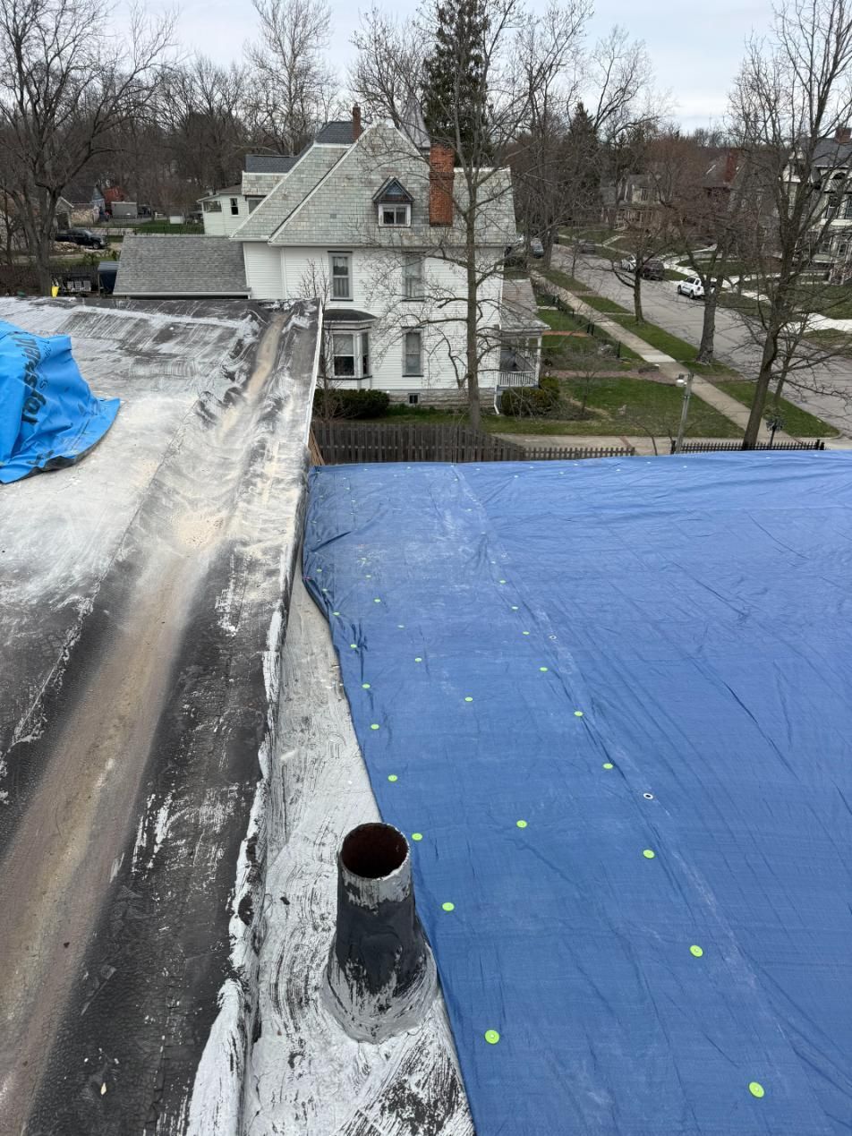 Rooftop with blue tarp, vent pipe, and a residential house and street in the background