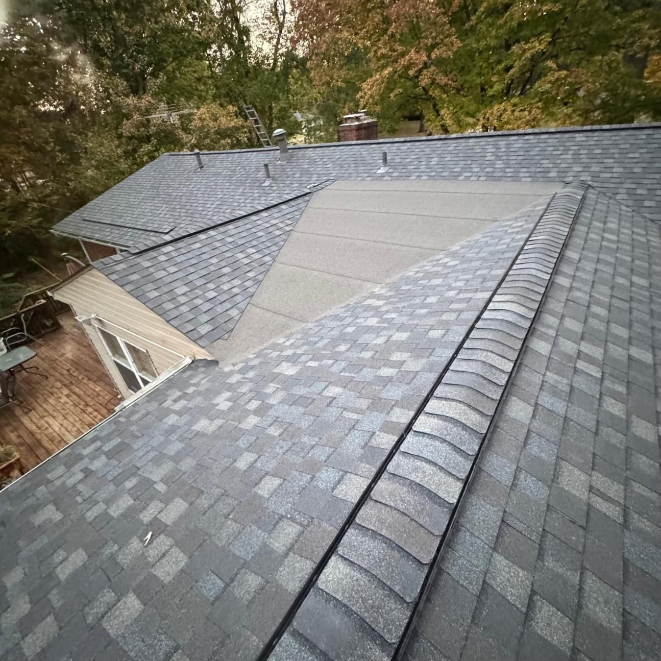 Residential roof with gray shingles and a visible patch repair, viewed from above among trees