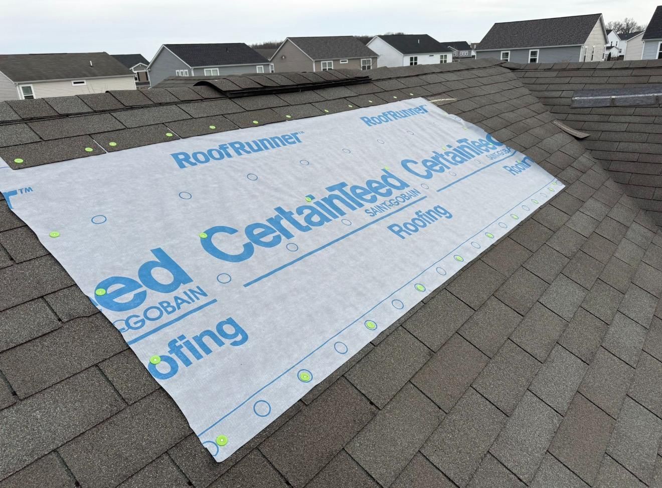 Roof underlayment installed on a sloped shingle roof with neighboring houses in the background