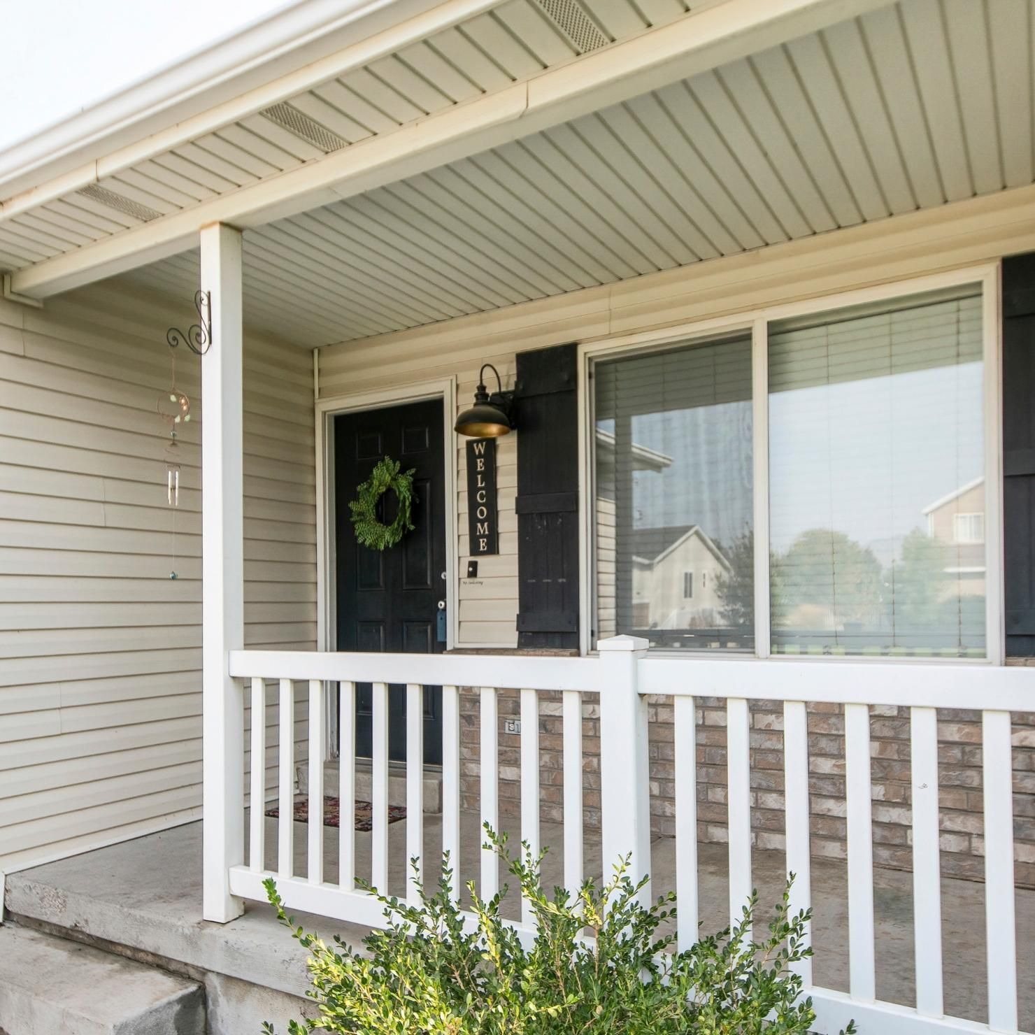 Covered front porch with white railing, black door, hanging lantern, and large window on a beige house.