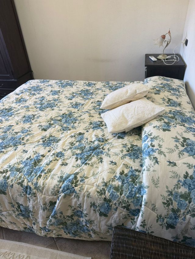 Camera da letto con copriletto a fiori, due cuscini e comodino accanto al letto.