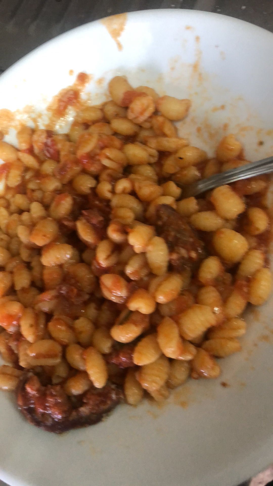 Un piatto di fagioli in salsa con un cucchiaio e qualche pezzetto di carne rosolata a parte.