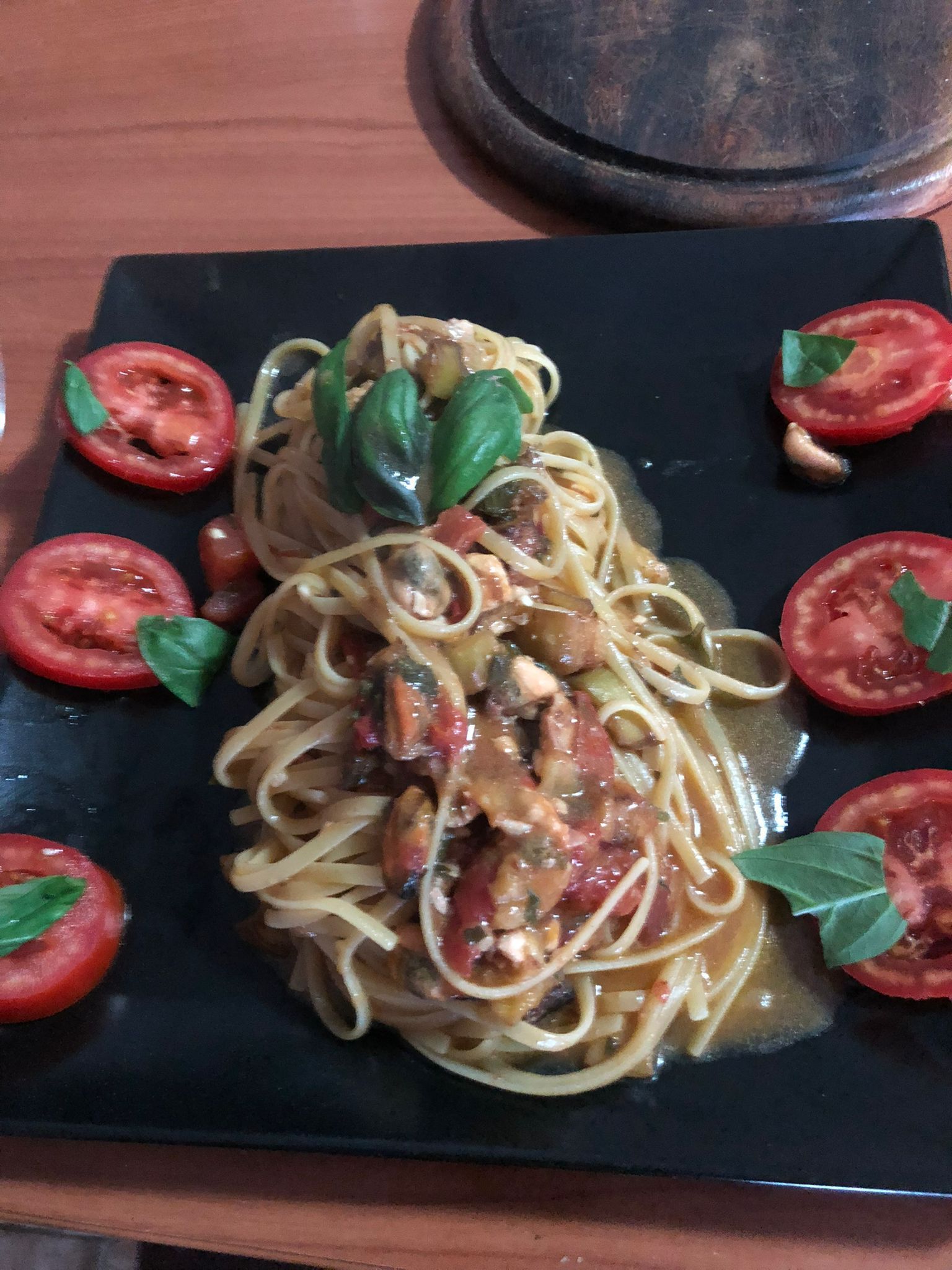 Spaghetti al sugo di pomodoro e basilico, guarniti con fette di pomodoro e serviti su un piatto quadrato nero.