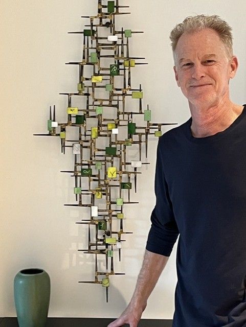 Man standing beside a modern abstract wall sculpture with green and yellow accents Man standing beside a geometric metal wall sculpture with green and yellow accents
