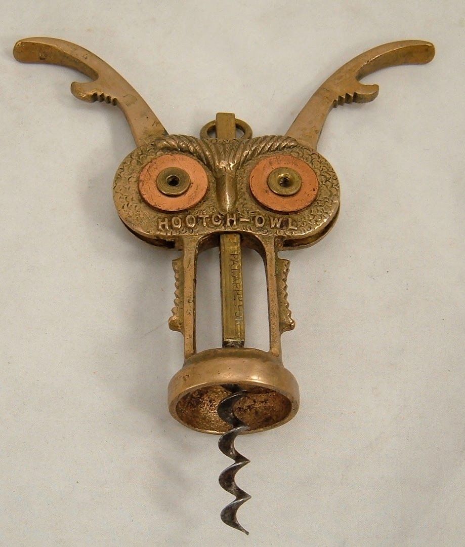 Close-up of a whimsical brass owl-shaped corkscrew with curled metal wings and spiral screw