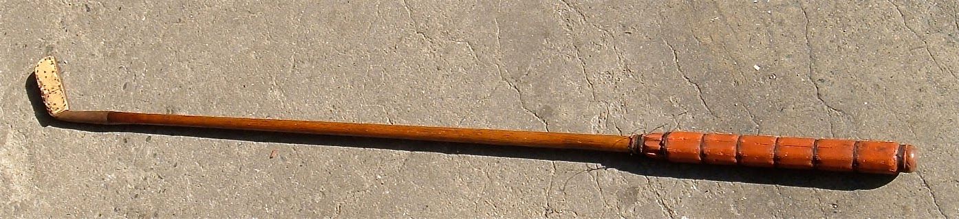 Wooden walking stick with a curved handle and orange-brown wrapped grip on a beige background