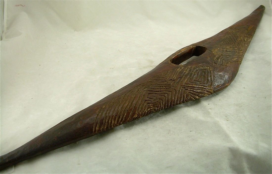 Brown wooden tribal mask with a long pointed nose and a small eye opening on a light cloth background