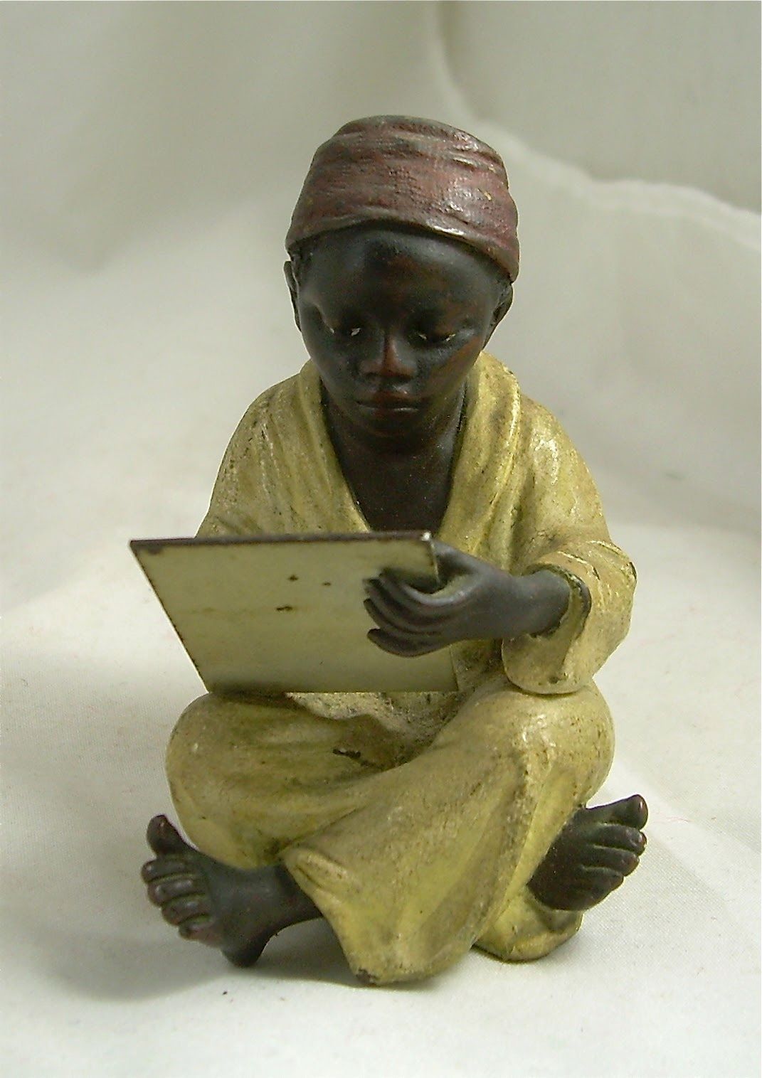 Small figurine of a seated child in yellow clothing holding a tablet or book