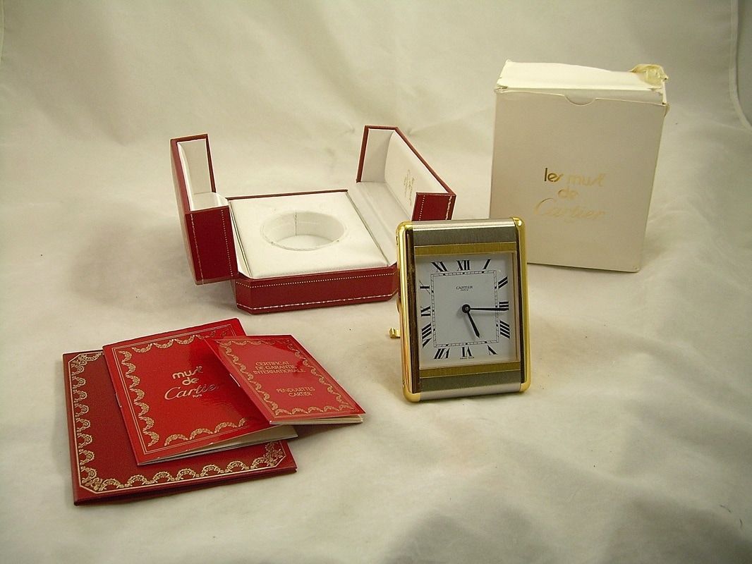 Red jewelry boxes and a gold clock arranged on a white cloth background