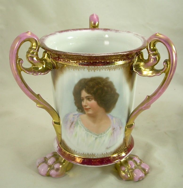Decorative porcelain vase with gold handles, pink accents, and a painted portrait on the front