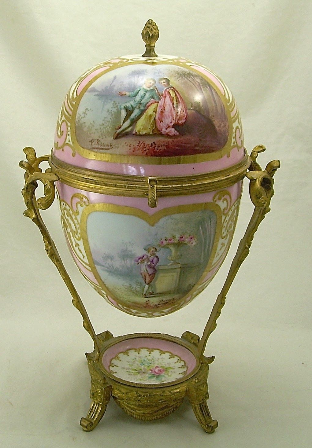 Ornate porcelain egg-shaped vase with gold trim and painted floral scenes on a stand