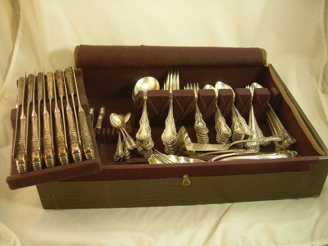 Open brown case with assorted silver cutlery and utensils arranged inside on a light background