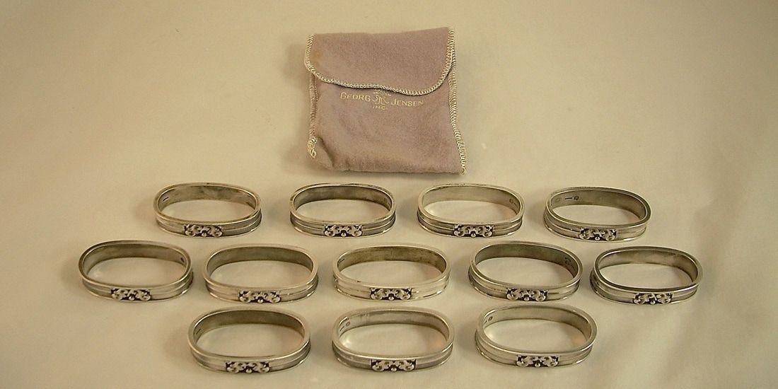 A pink pouch above ten silver rings arranged on a beige background