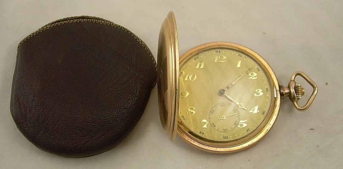 Open gold pocket watch with white face beside a dark round case on a white background