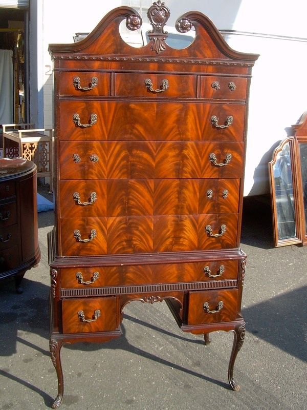 Antique wooden chest of drawers with ornate top and curved legs at an outdoor market