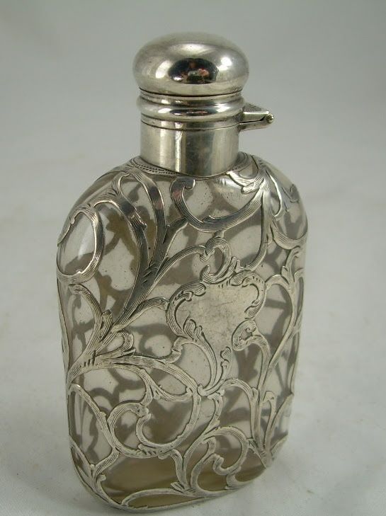 Silver decorative perfume bottle with ornate floral cutout design and rounded cap