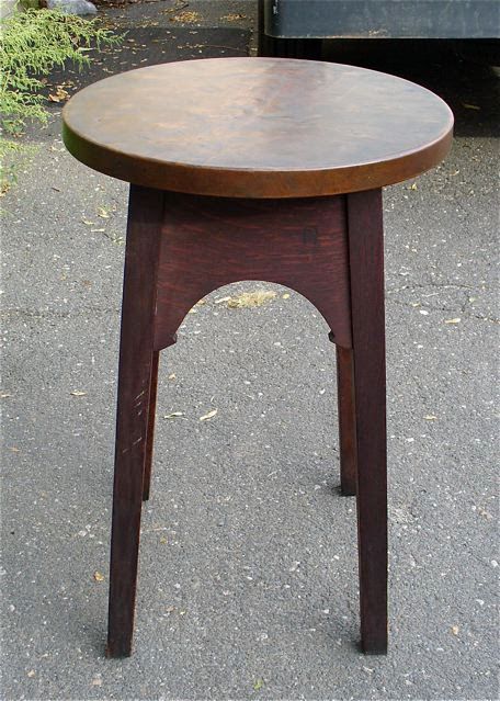 Round wooden stool with dark legs and a brown seat on pavement.