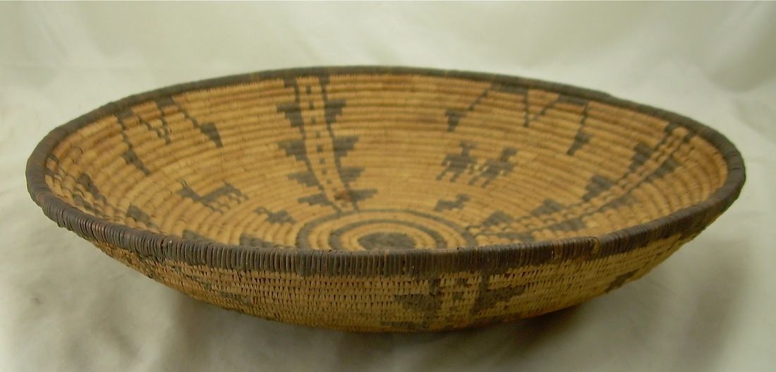 Shallow woven basket with tan and black geometric patterns on a plain background