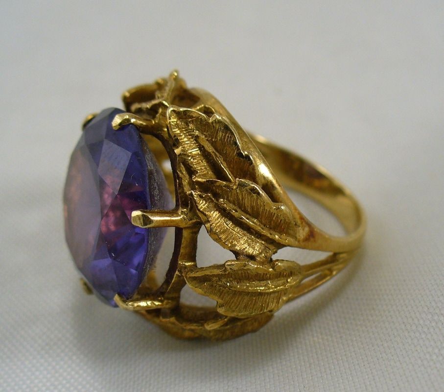 Gold ring with a large oval purple gemstone and leaf-shaped details