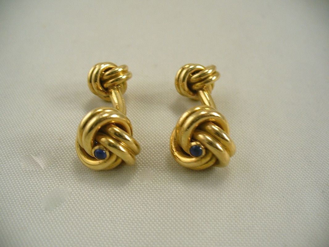 Pair of gold knot earrings with small blue accents on a light background
