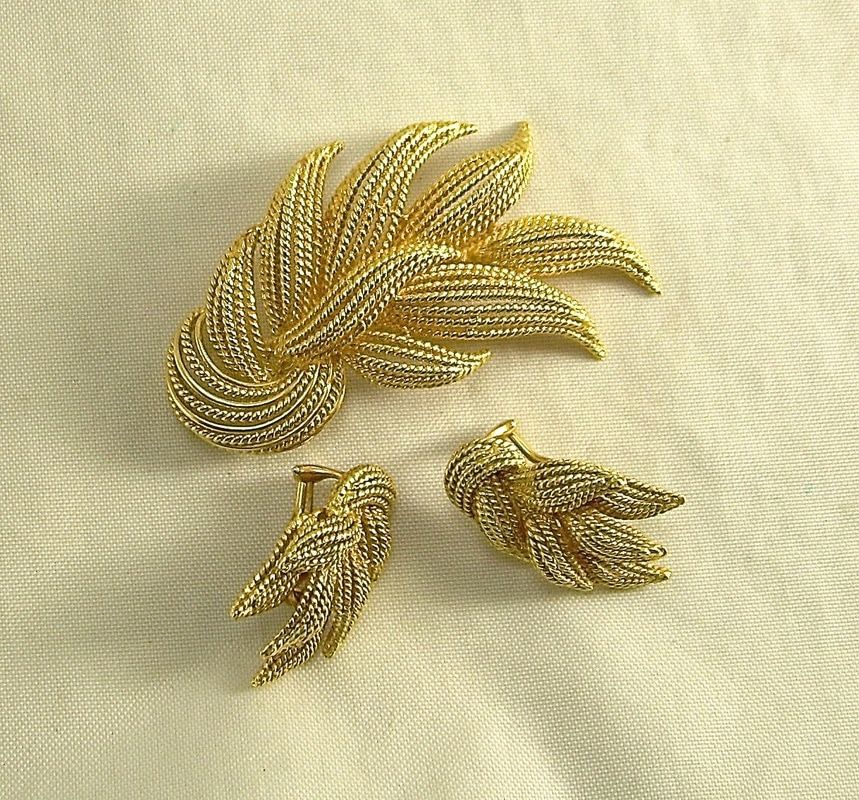 Gold leaf brooch with two matching leaf-shaped earrings on beige fabric background