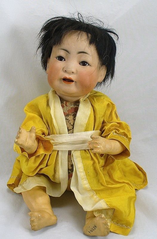 Small doll in a yellow robe sitting against a plain white background