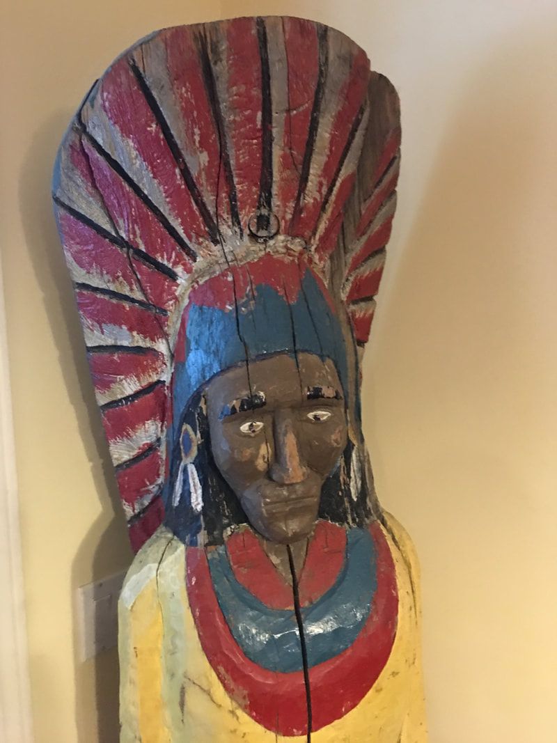 Colorful carved mask with tall red-and-blue headdress on a beige wall