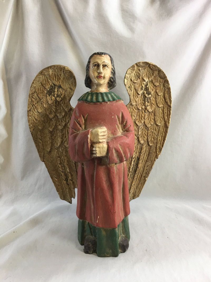 Small angel figurine with gold wings, pink robe, and clasped hands against a white cloth background