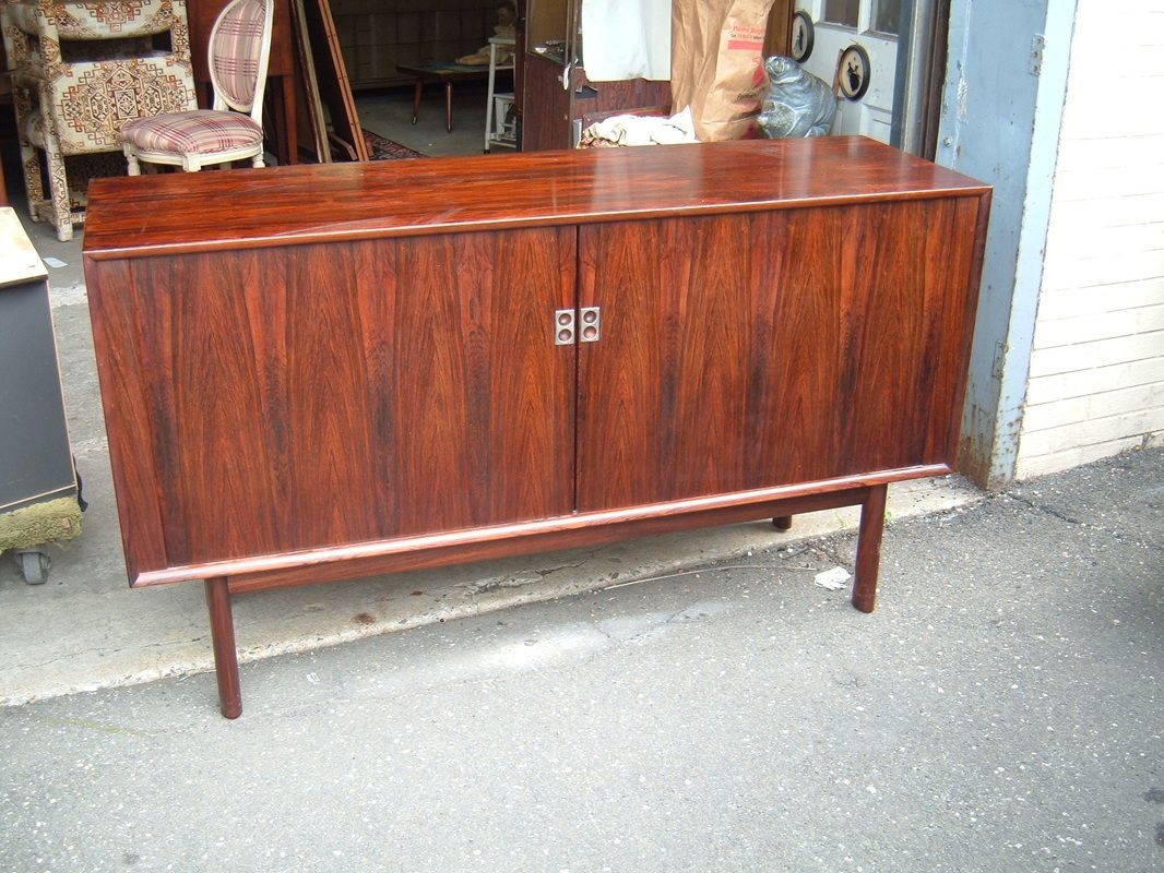 Wooden cabinet with brown finish standing outside on a sidewalk.