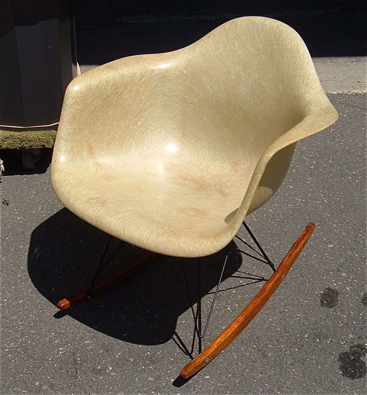 Beige molded chair with black wire legs and wooden rocker runners, shown outdoors on pavement.