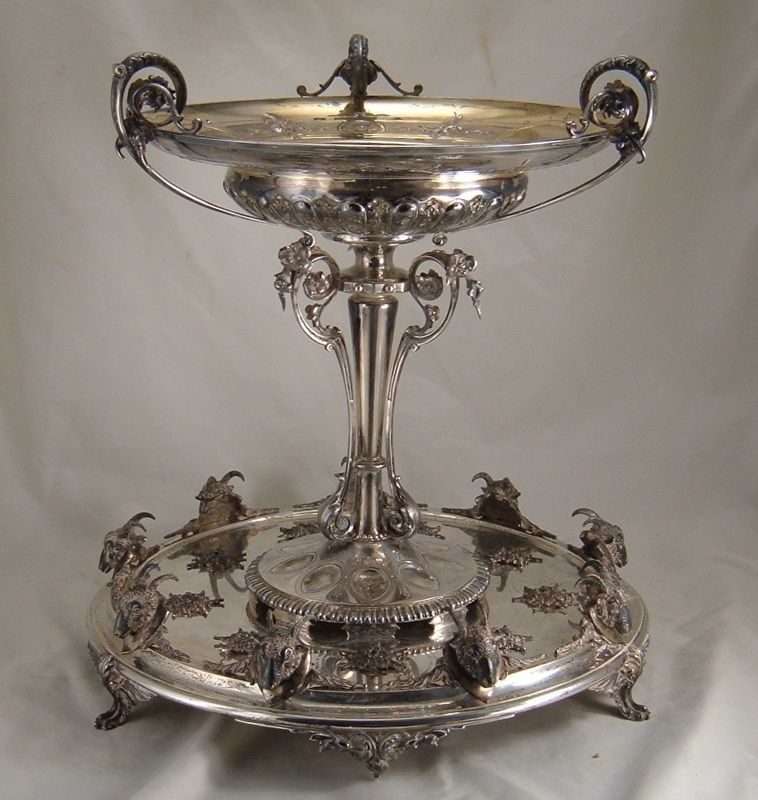 Ornate silver serving centerpiece with lid on a decorative stand, displayed against a plain background