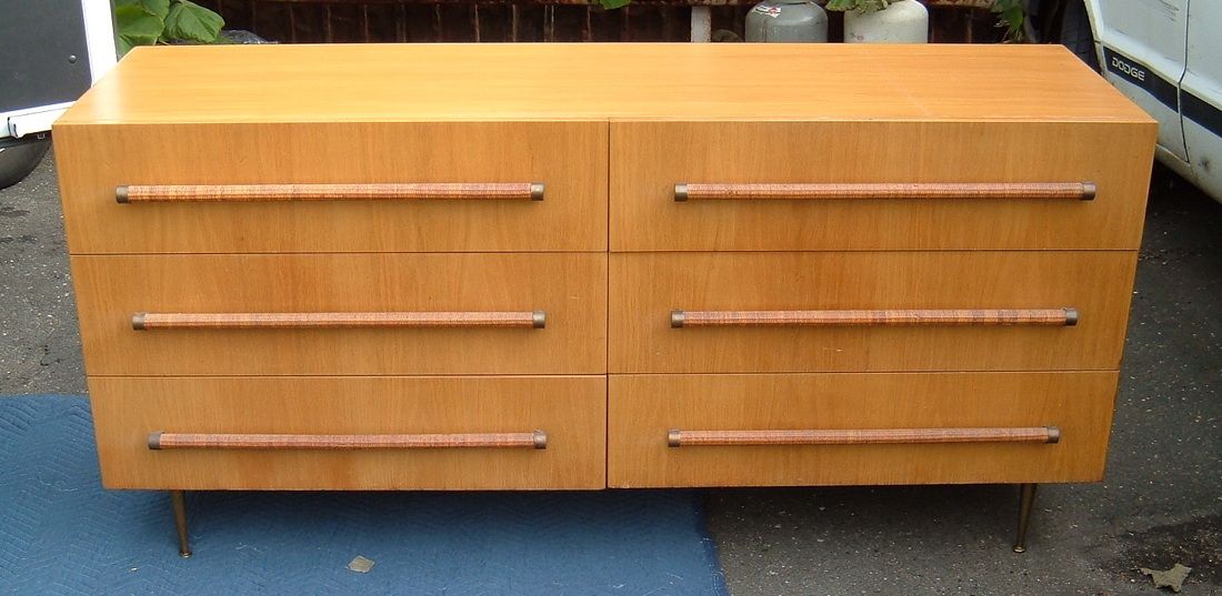 Orange wooden dresser with six drawers and long silver handles on short black legs
