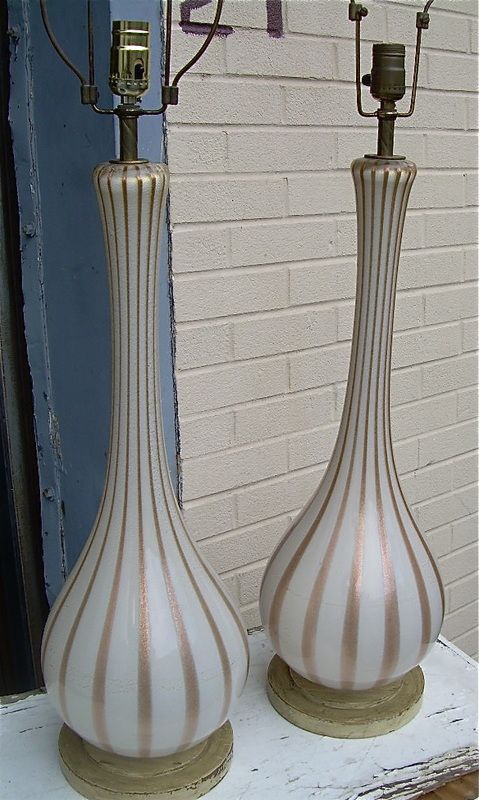 Two tall white-and-tan striped ceramic lamps or vases on a shelf against a white brick wall