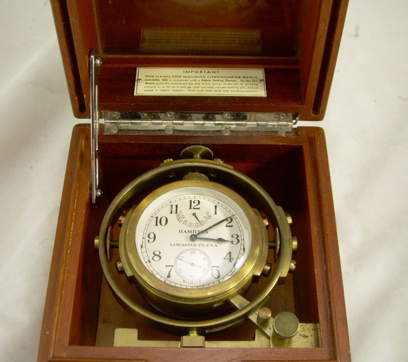 Antique brass clock in a polished wooden case, open to show the white clock face and internal mechanisms.